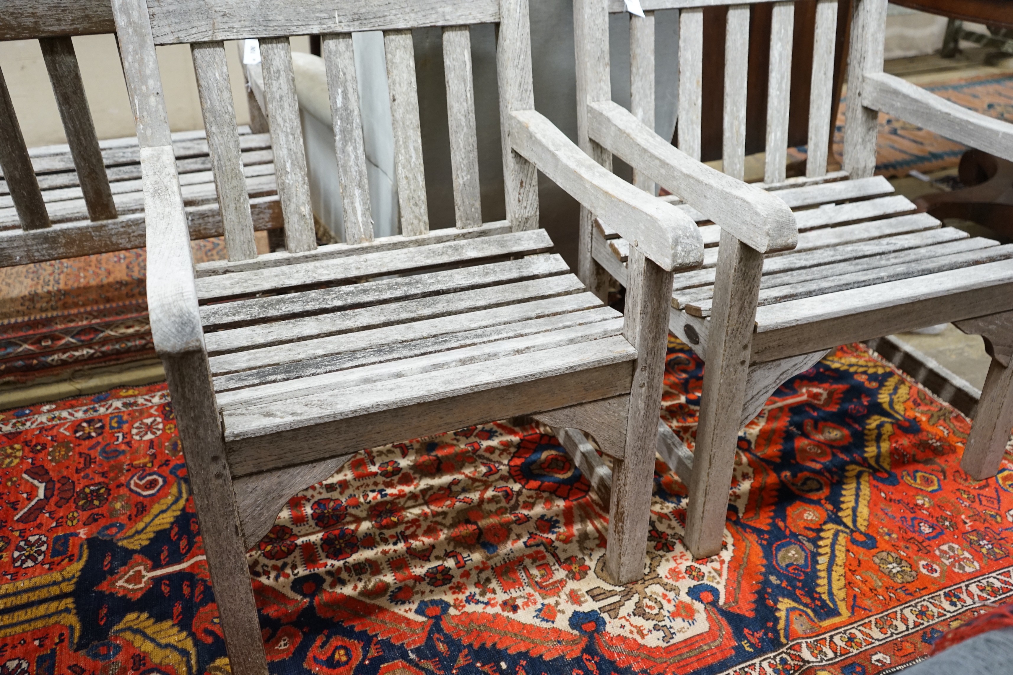 A pair of slatted weathered teak garden elbow chairs, width 60cm, depth 58cm, height 83cm